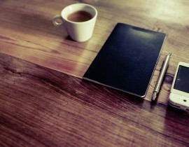 Šálka kávy, zápisník, pero a mobil na stole